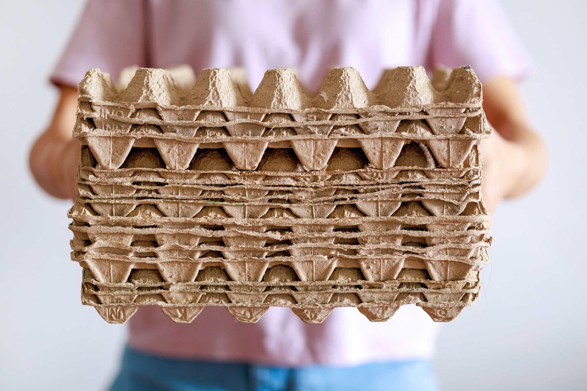 Cropped image of an Asian woman holding a pile of egg tray cardboard, ready for recycling, showcasing a sustainable lifestyle